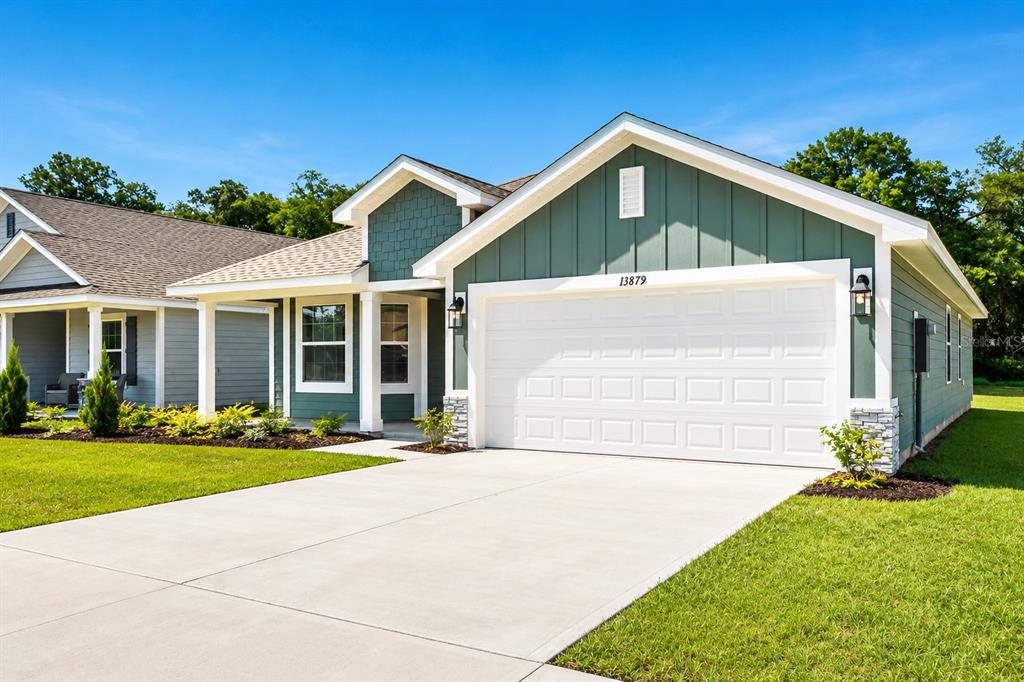 A single-story house with green siding, a white garage door, and a concrete driveway — 13879 NW 150TH CIRCLE, ALACHUA, FL