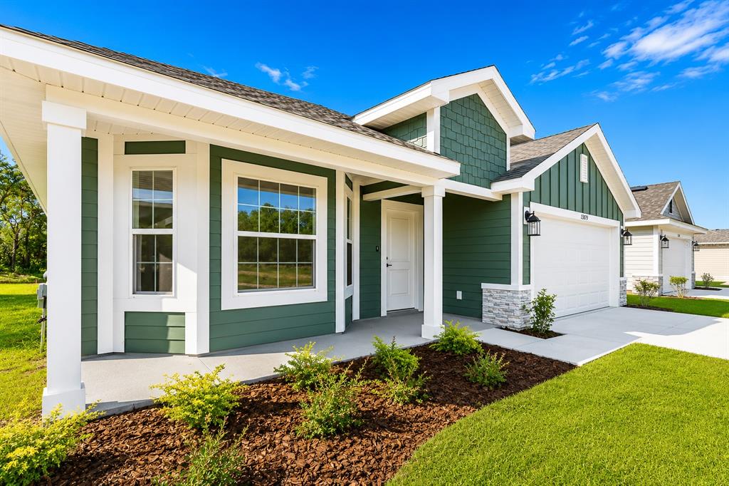 A green-sided house with a white garage, covered porch, and landscaped front yard — 13879 NW 150TH CIRCLE, ALACHUA, FL