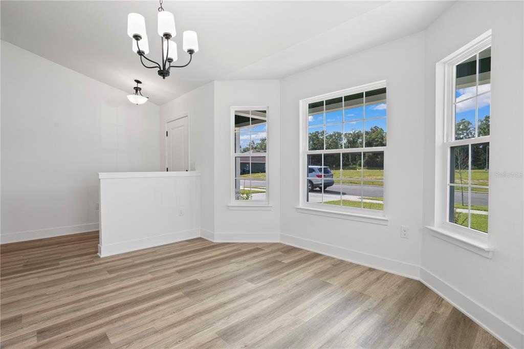 A bright dining area with wood-look flooring, a chandelier, and windows overlooking a neighborhood street — 13879 NW 150TH CIRCLE, ALACHUA, FL