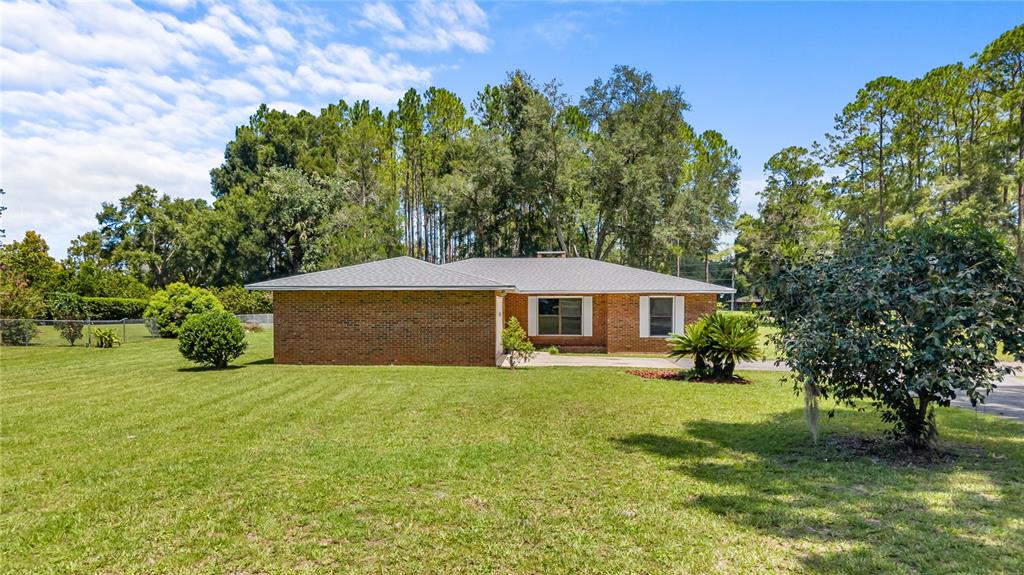 A single-story brick house with a gray roof sits on a large, grassy lawn — 1108 SW 2ND AVENUE, CHIEFLAND, FL