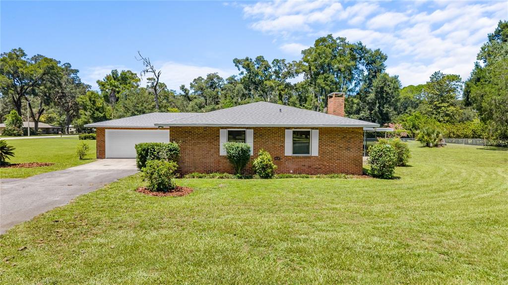 A single-story brick house with a gray roof, attached garage, and a large grassy yard — 1108 SW 2ND AVENUE, CHIEFLAND, FL