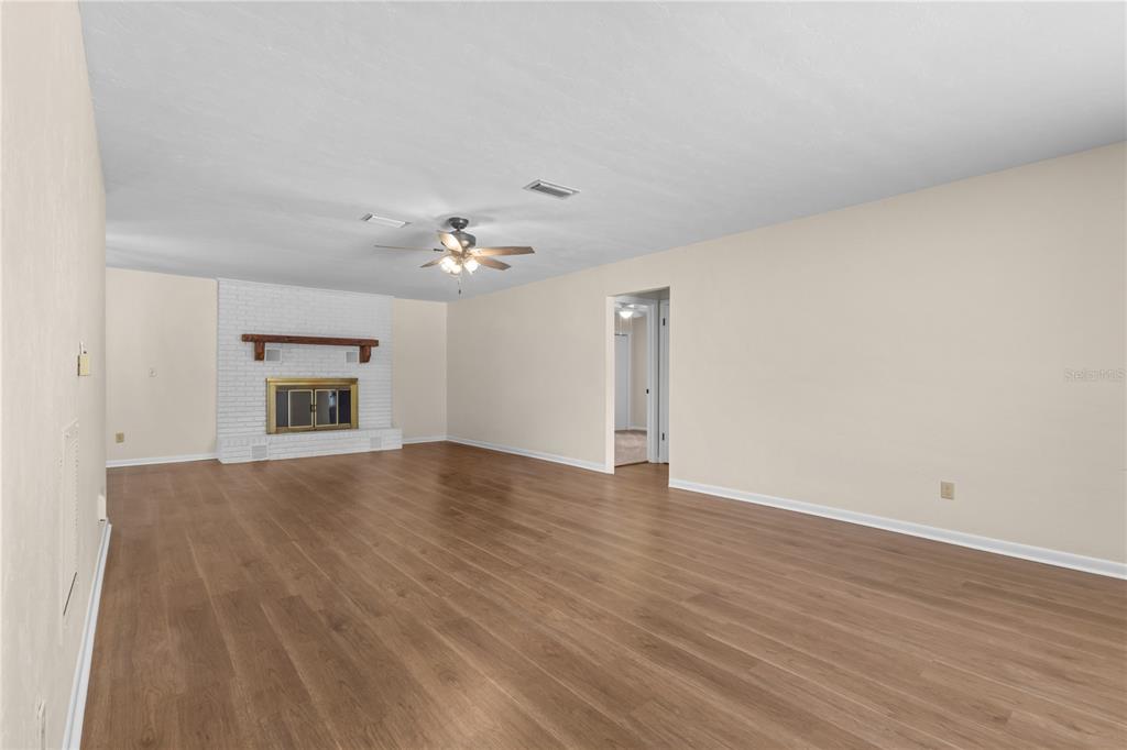 An empty living room features wood-look flooring, a white brick fireplace, and a ceiling fan — 1108 SW 2ND AVENUE, CHIEFLAND, FL