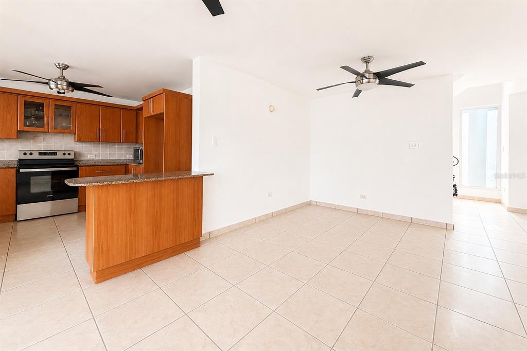 A kitchen with wood cabinets, stainless steel appliances, granite countertops, and beige tile flooring — Estancias de Cerro Gordo N CALLE NINOSHKA UNIT B-12, VEGA ALTA, PR