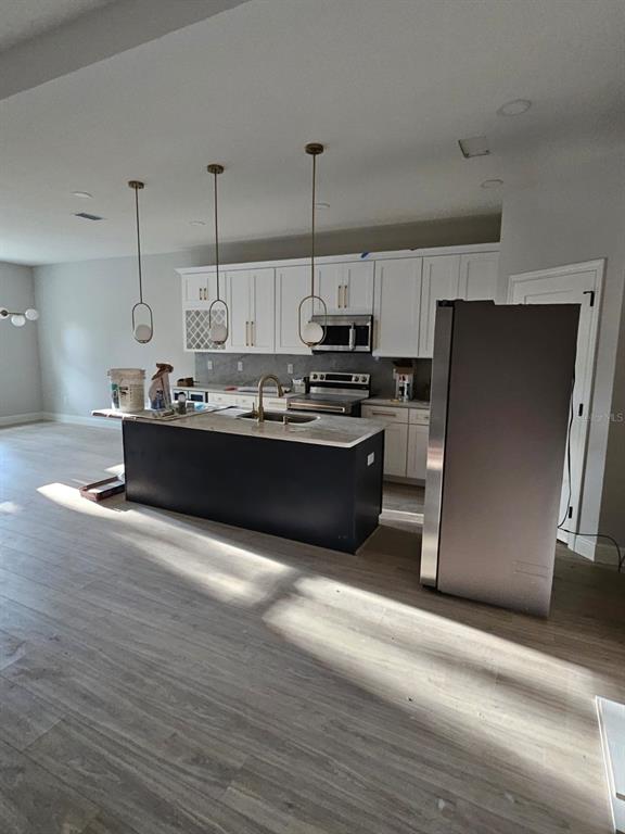 A kitchen features a dark island, white cabinetry, stainless steel appliances, and light wood flooring — 13105 N BOULEVARD, TAMPA, FL