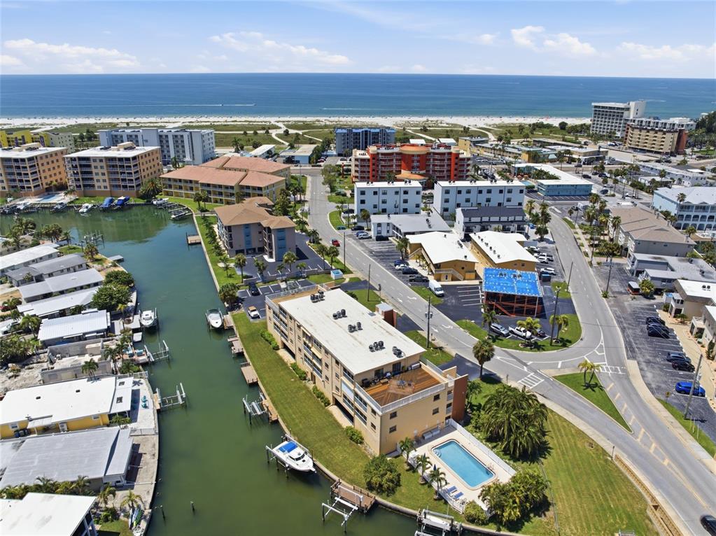 An aerial view shows a multi-story apartment building with a pool beside a canal — 175 116TH AVENUE UNIT 206, TREASURE ISLAND, FL