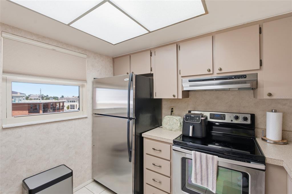 A kitchen features stainless steel appliances, light-colored cabinets, a window with a view, and tile flooring — 175 116TH AVENUE UNIT 206, TREASURE ISLAND, FL