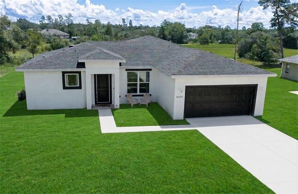A single-story white house with a dark roof, black garage door, and a green lawn — 16373 SW 48TH CIRCLE, OCALA, FL