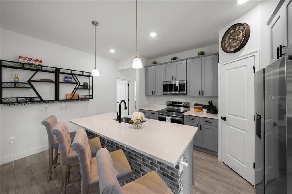 A modern kitchen features a central island with bar seating, gray cabinetry, and brick accents — 16373 SW 48TH CIRCLE, OCALA, FL