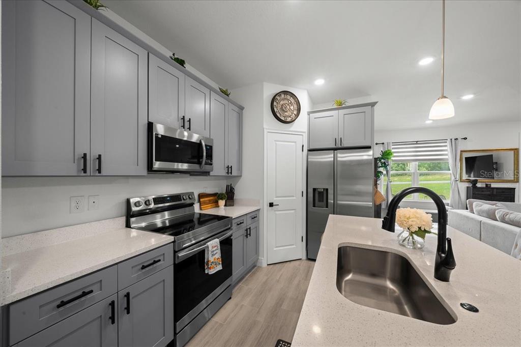 A modern kitchen features gray cabinets, stainless steel appliances, a quartz island, and wood-look flooring — 16373 SW 48TH CIRCLE, OCALA, FL
