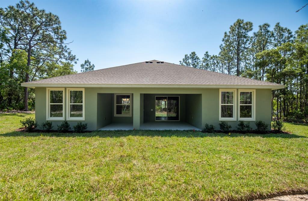 The back exterior of a single-story house features a covered patio and a grassy yard — 1834 NW 79TH LOOP, OCALA, FL