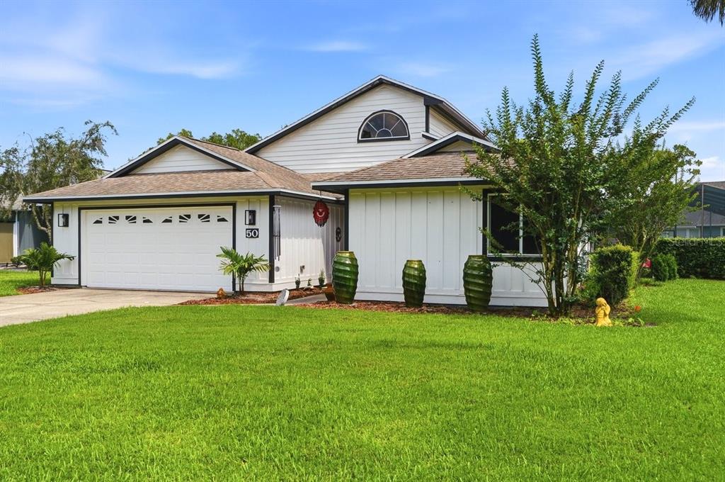 A white house with a two-car garage and three large green planters in the front — 50 TREETOP CIRCLE, ORMOND BEACH, FL