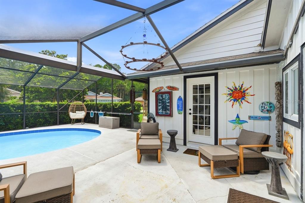 A screened-in patio features a swimming pool, outdoor furniture, and decorative wall art — 50 TREETOP CIRCLE, ORMOND BEACH, FL