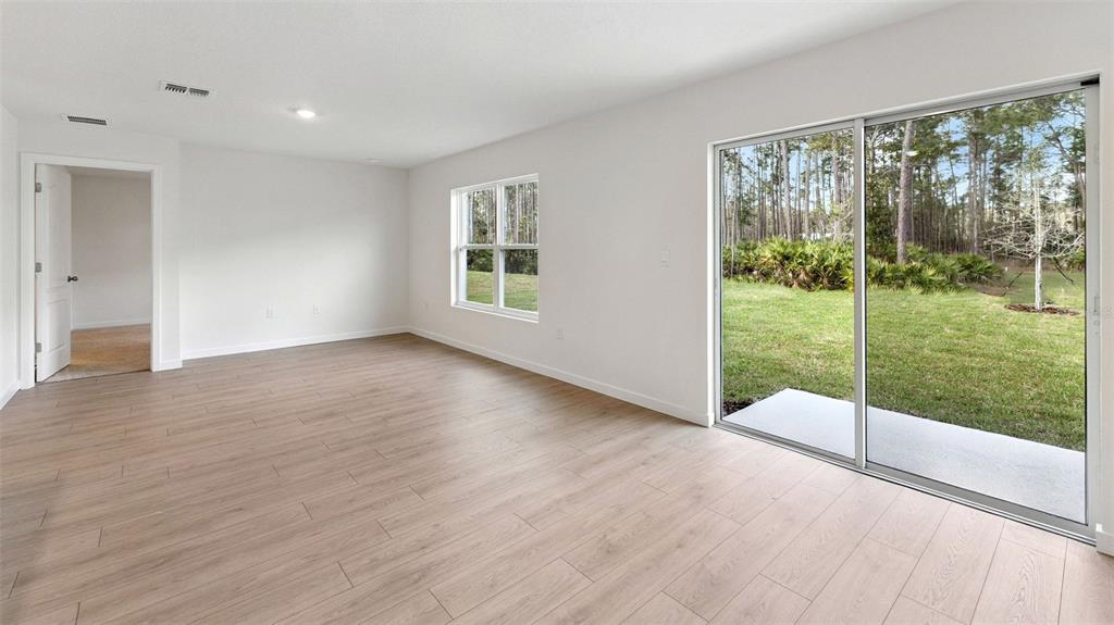 An empty room with light wood-look flooring, a sliding glass door, and a backyard view — 139 HEIRLOOM DRIVE, ORMOND BEACH, FL