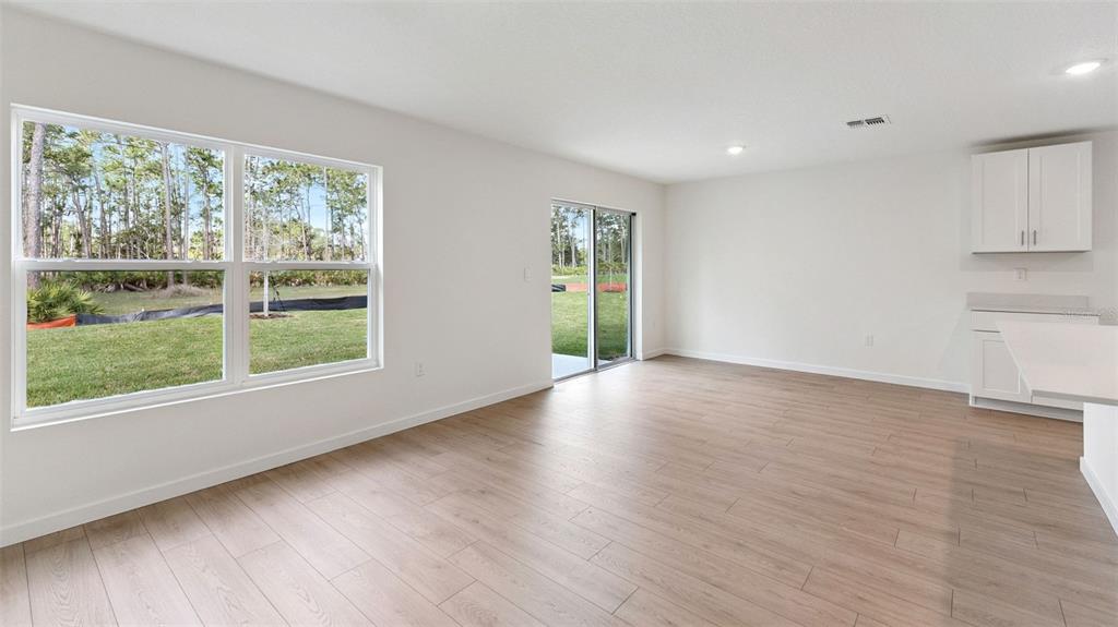 A bright living area features light wood-look flooring, white walls, and a sliding glass door — 139 HEIRLOOM DRIVE, ORMOND BEACH, FL