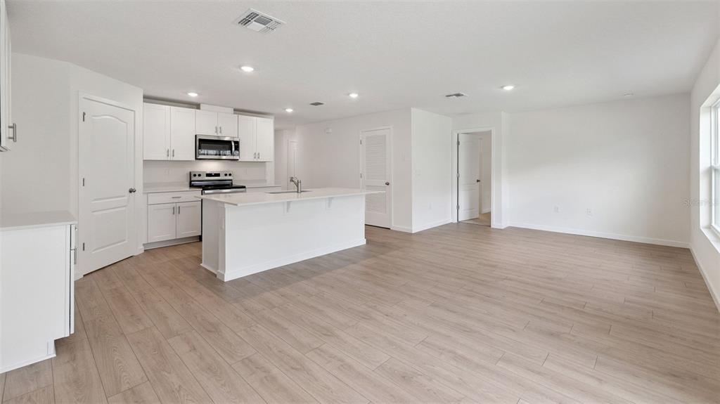 A bright kitchen with white cabinets and a center island opens into a living area — 139 HEIRLOOM DRIVE, ORMOND BEACH, FL