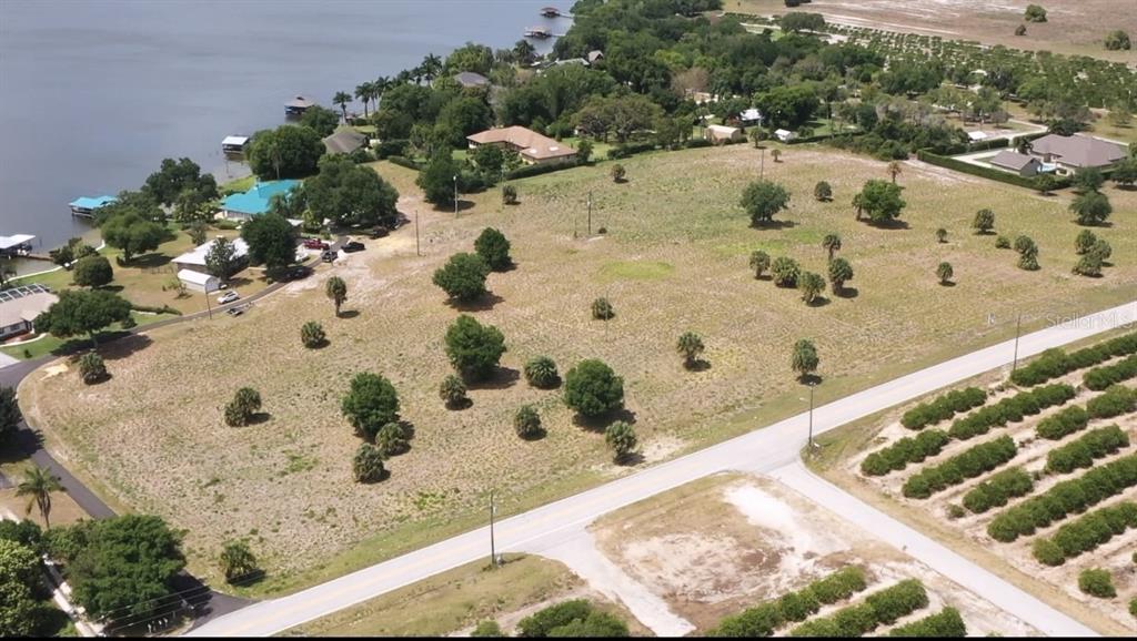 An aerial view shows a large, grassy vacant lot situated next to a lake — 70 CATFISH LANE, LAKE PLACID, FL