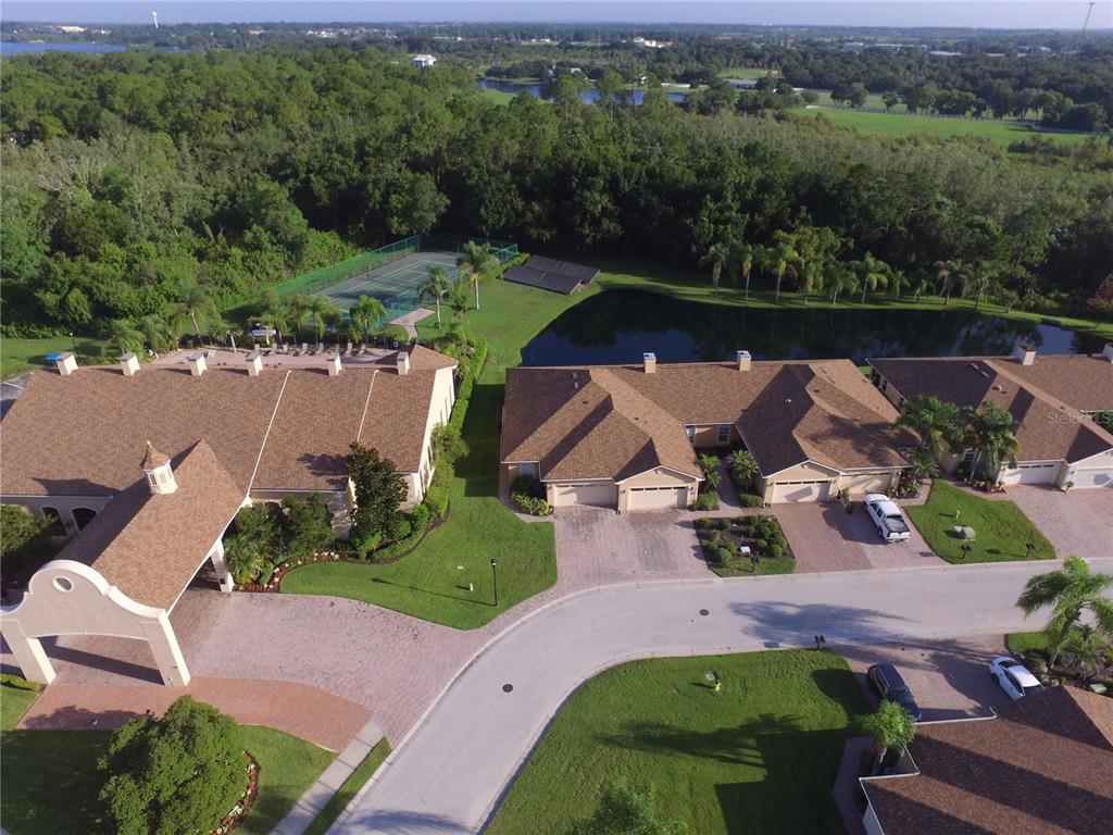 An aerial view shows a residential complex with a pond, tennis court, and paved driveways — 1307 INNSBRUCK CT, WINTER HAVEN, FL