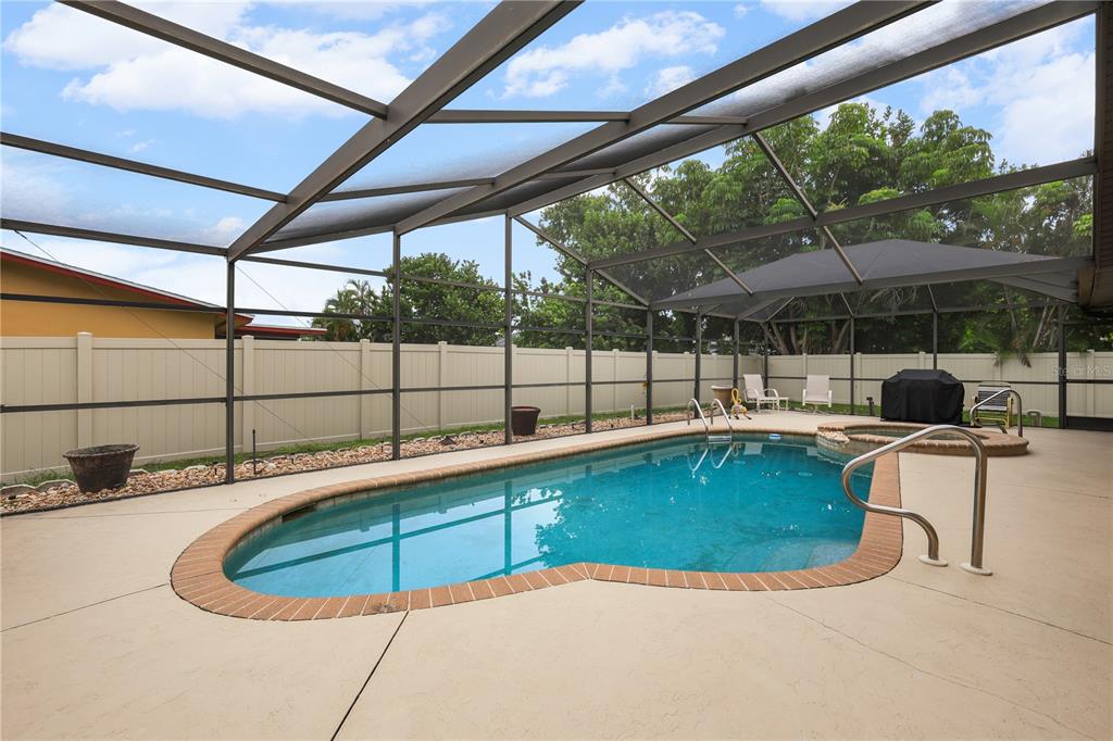 A screened-in backyard features a swimming pool with a brick border and a hot tub — 4029 COUNTRY CLUB BOULEVARD, CAPE CORAL, FL