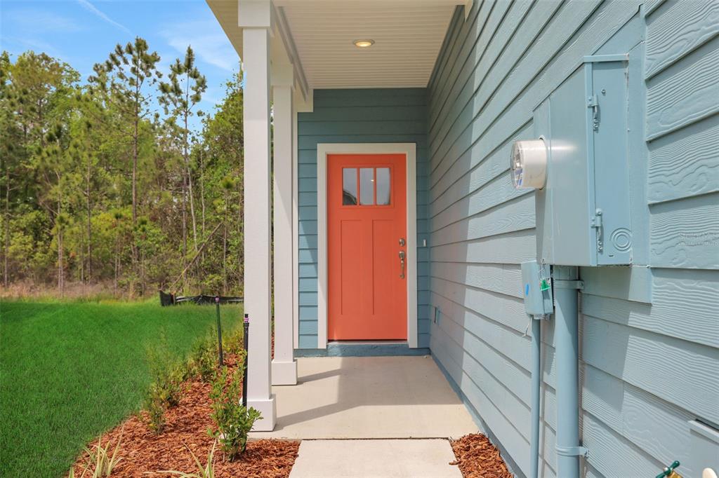 A bright orange front door is set against light blue siding on a covered porch — 3779 ATHENIAN WAY, MIDDLEBURG, FL