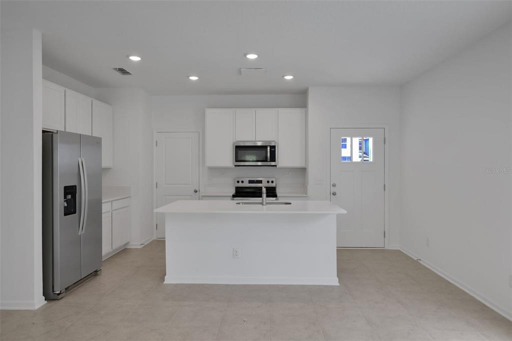 A modern kitchen features white cabinets, stainless steel appliances, a center island, and tile flooring — 3779 ATHENIAN WAY, MIDDLEBURG, FL