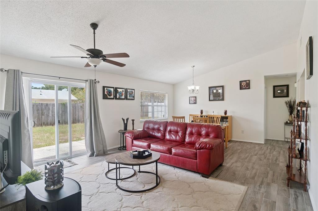 A living room with a red leather sofa, wood-look flooring, and a sliding glass door — 1919 DEANNA DRIVE, APOPKA, FL