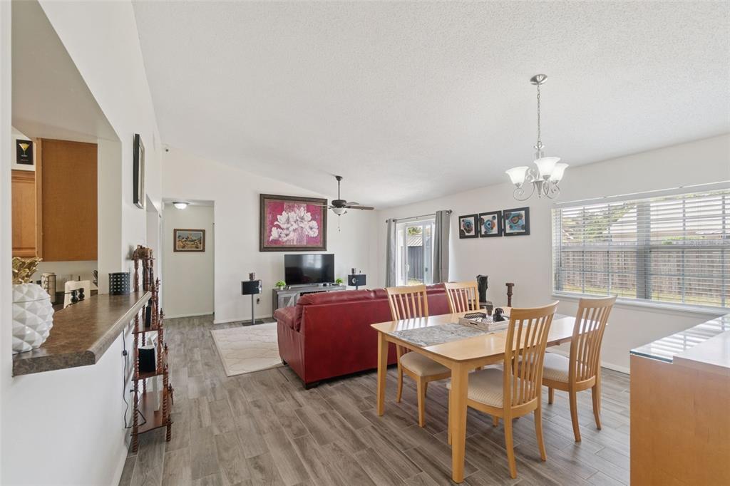 An open-concept living and dining area features wood-look tile flooring and a red sofa — 1919 DEANNA DRIVE, APOPKA, FL