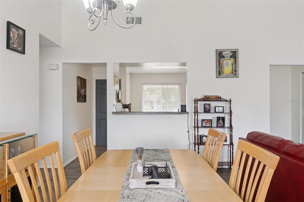 A dining room features a wooden table, chairs, a chandelier, and a kitchen pass-through window — 1919 DEANNA DRIVE, APOPKA, FL
