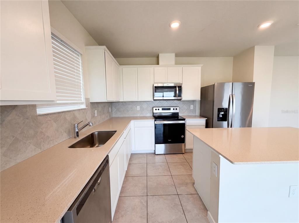 A kitchen features white cabinets, stainless steel appliances, a kitchen island, and tiled flooring — 7768 SYRACUSE DRIVE, CLERMONT, FL
