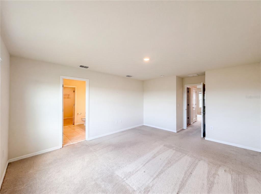 An empty bedroom with beige carpet, neutral walls, and two doorways leading to other rooms — 7768 SYRACUSE DRIVE, CLERMONT, FL