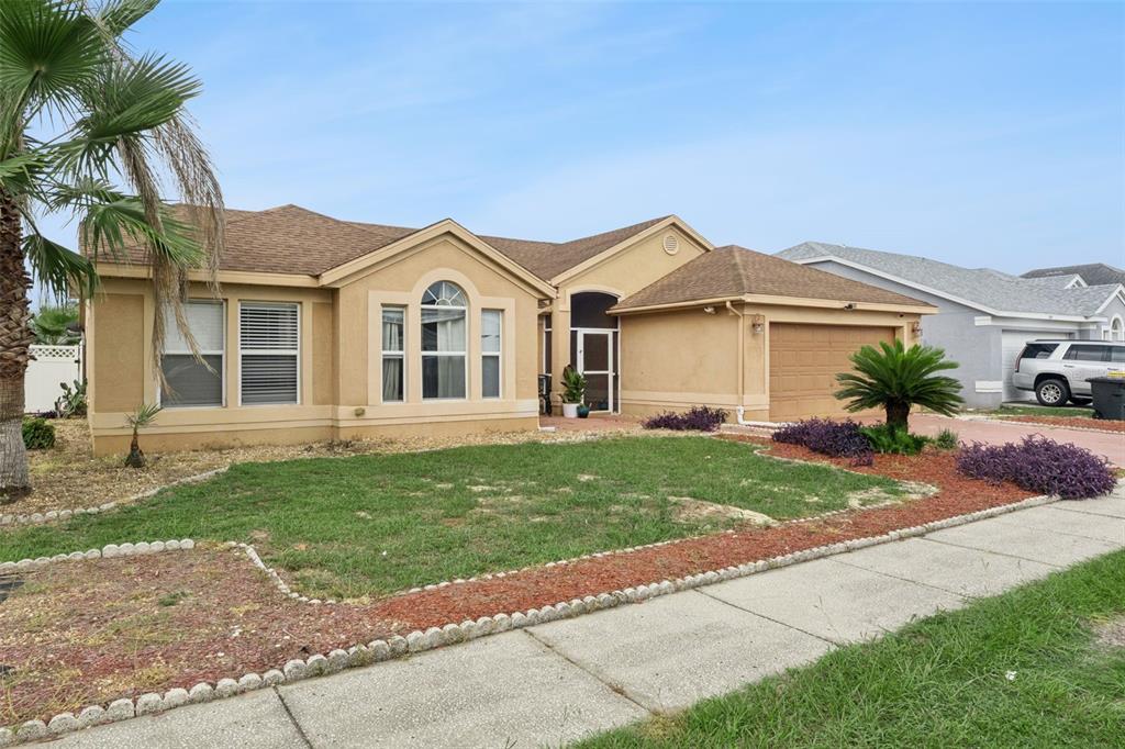 A tan single-story house with a brown shingled roof, a two-car garage, and landscaping — 8611 PRIMROSE DRIVE, KISSIMMEE, FL