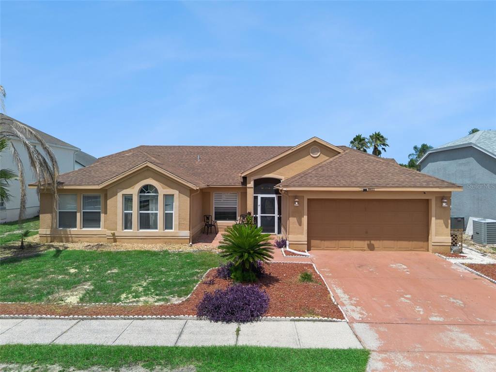 A single-story tan stucco house with a brown shingled roof and a two-car garage — 8611 PRIMROSE DRIVE, KISSIMMEE, FL