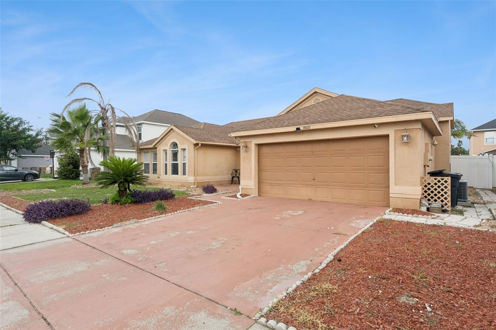 A single-story house with a tan stucco exterior, a two-car garage, and a paved driveway — 8611 PRIMROSE DRIVE, KISSIMMEE, FL