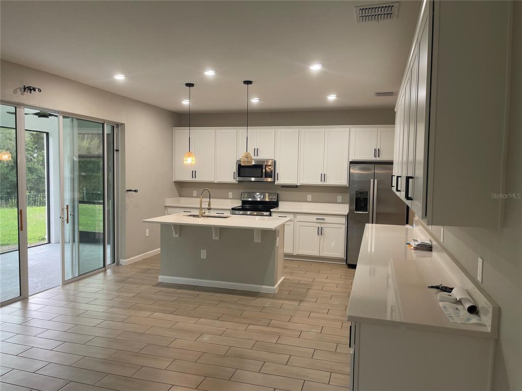 A modern kitchen features white cabinets, a central island with a sink, and tile flooring — 2994 GAVIN SKY DRIVE, KISSIMMEE, FL