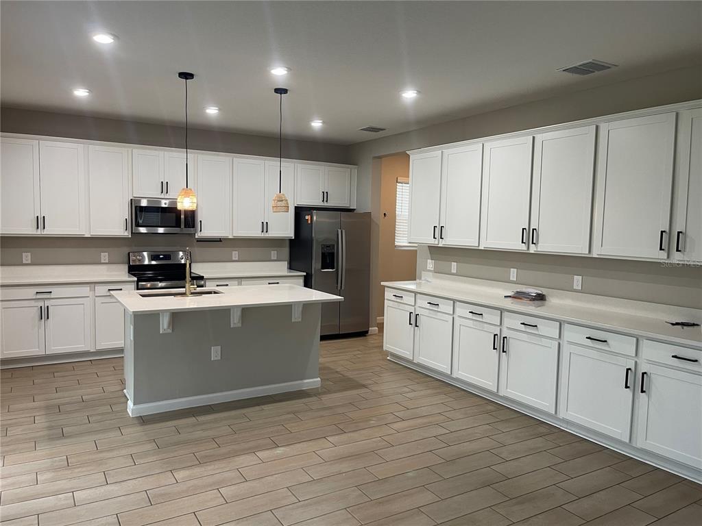 A modern kitchen features white cabinetry, stainless steel appliances, a center island, and wood-look flooring — 2994 GAVIN SKY DRIVE, KISSIMMEE, FL