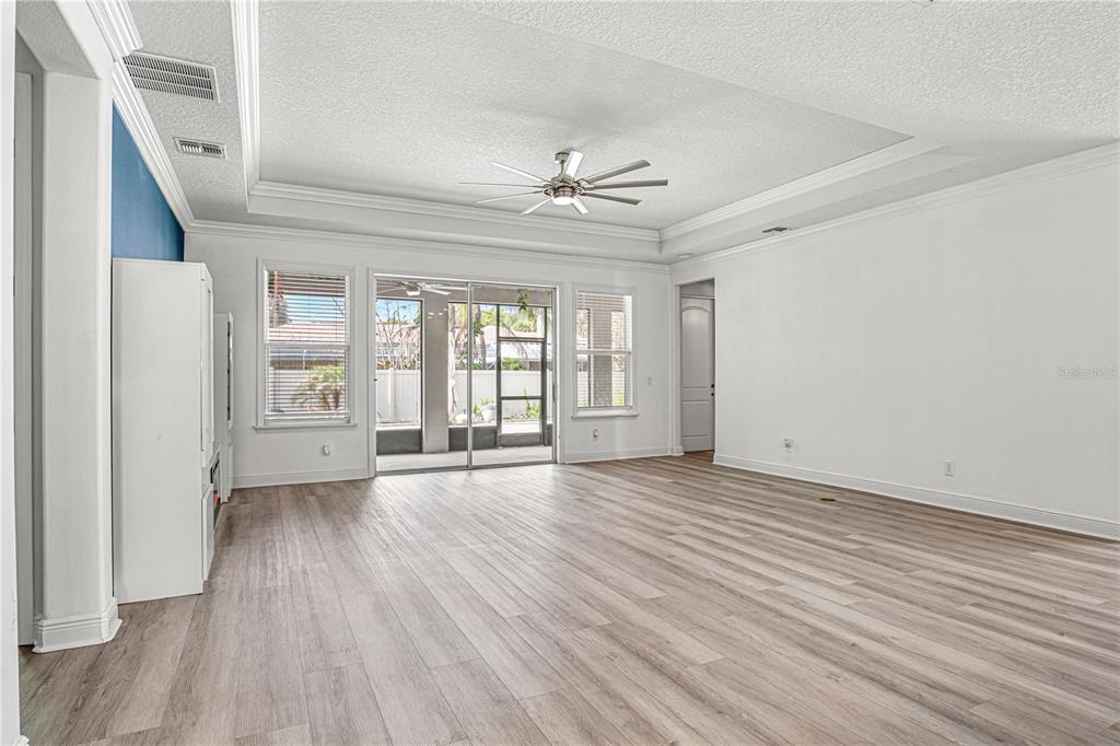 A spacious living room features light wood-look flooring, a tray ceiling, and sliding glass doors — 1772 KILLIAN DRIVE NE, PALM BAY, FL