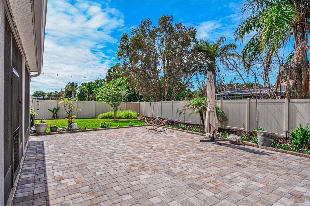 A paved patio sits in a fenced backyard with a lawn and mature trees — 1772 KILLIAN DRIVE NE, PALM BAY, FL