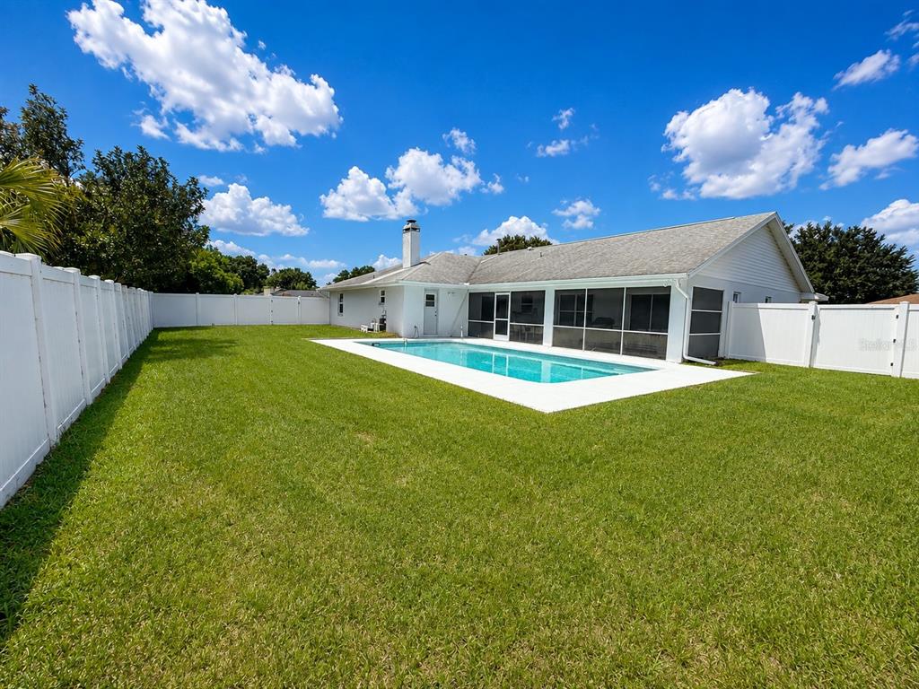 A backyard features a rectangular swimming pool, a screened-in patio, and a white privacy fence — 204 LAKE MARIAM COURT, WINTER HAVEN, FL