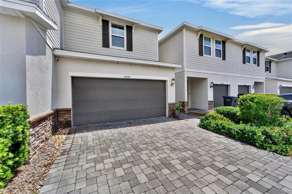 A two-story townhouse exterior features a paver driveway, a gray garage door, and siding — 15037 ABBY BIRCH PLACE, TAMPA, FL