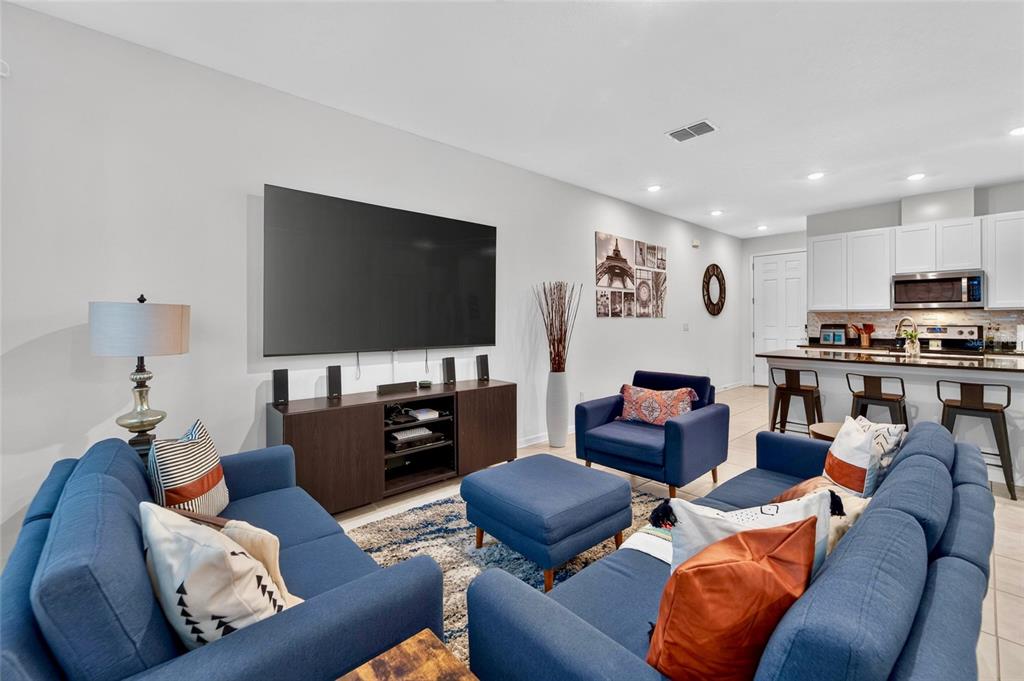 A living room features blue sofas, a large television, and an open kitchen with bar stools — 15037 ABBY BIRCH PLACE, TAMPA, FL