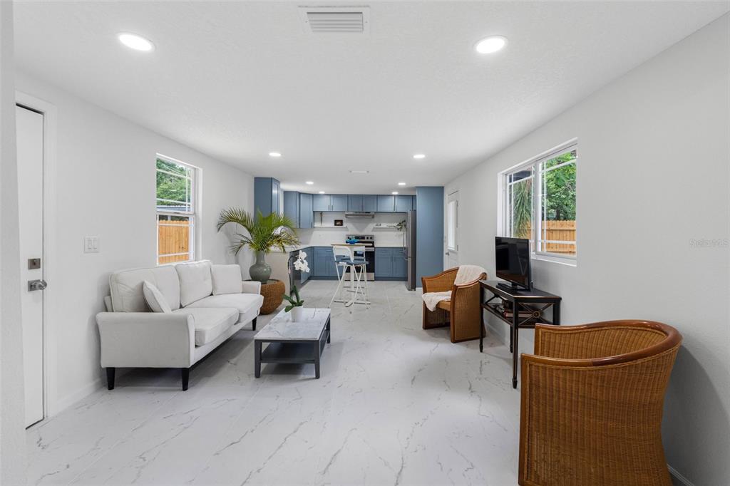 A white house exterior features a wooden deck, a dark front door, and gravel landscaping — 1208 E CHILKOOT AVENUE, TAMPA, FL