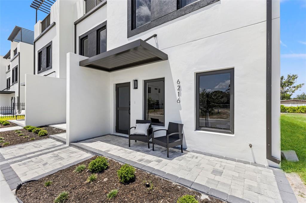 A modern white townhouse exterior features a paved entryway, a dark awning, and two chairs — 6216 64TH WAY N, PINELLAS PARK, FL