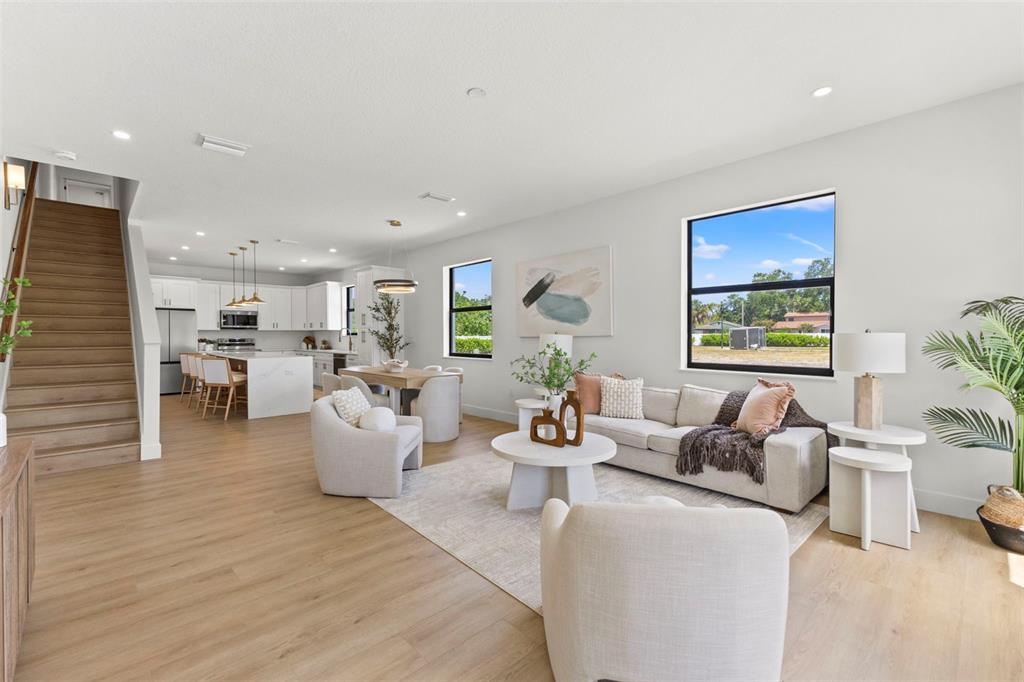 An open-concept living room and kitchen feature light wood flooring, white cabinetry, and a staircase — 6216 64TH WAY N, PINELLAS PARK, FL