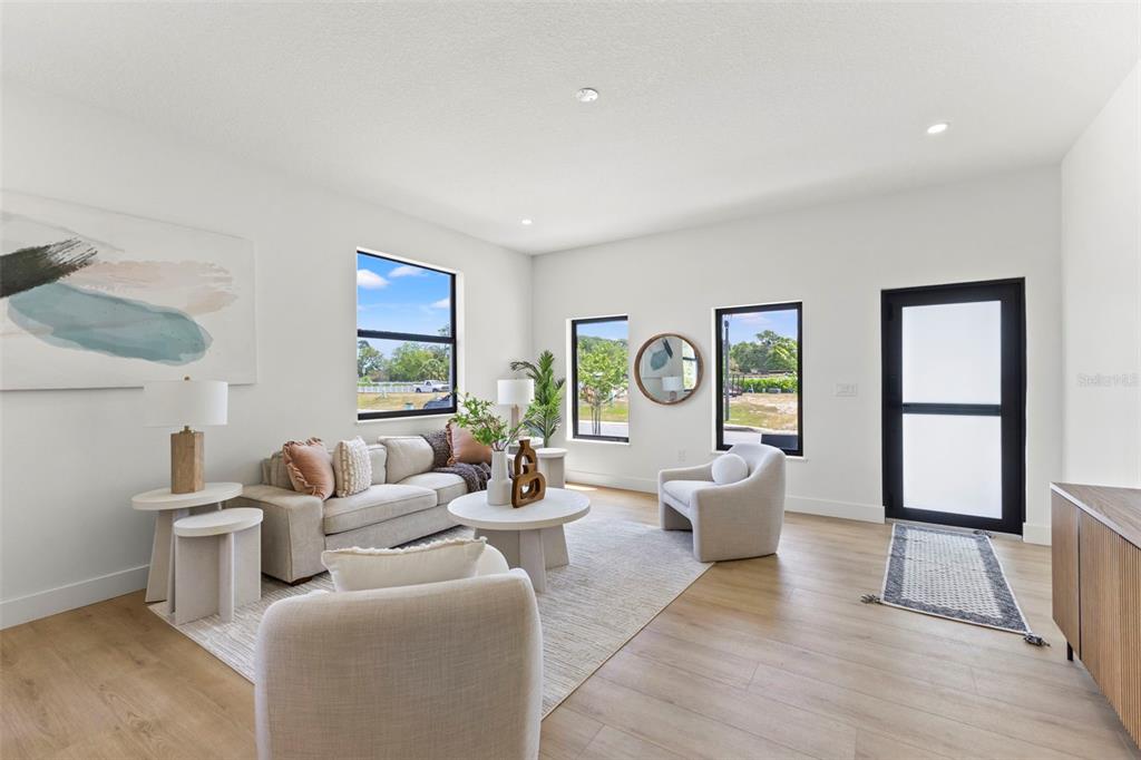 A bright living room features light wood flooring, neutral furniture, and a black-framed glass door — 6216 64TH WAY N, PINELLAS PARK, FL