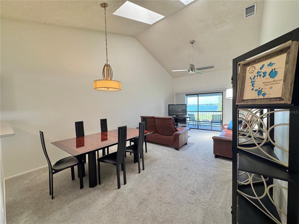 A dining area and living room with vaulted ceilings, carpeted floors, and a lake view — 715 MAGNOLIA PLACE UNIT 715, WINTER HAVEN, FL