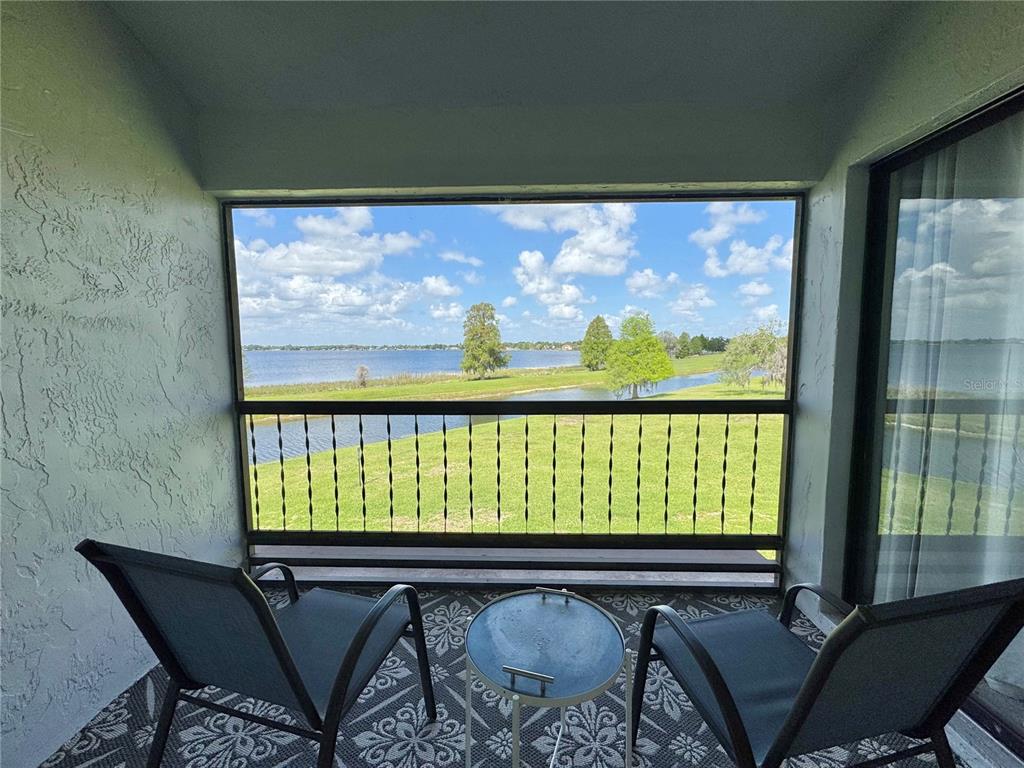 A screened balcony features two chairs, a small table, and a view of a lake — 715 MAGNOLIA PLACE UNIT 715, WINTER HAVEN, FL