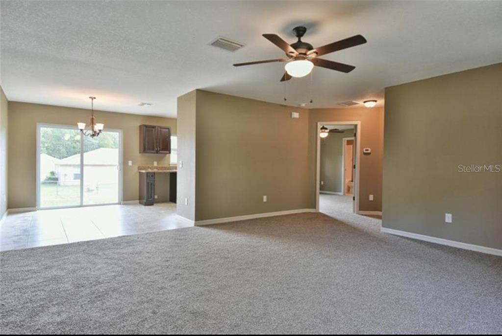 A living room with beige carpet and a ceiling fan opens to a tiled dining area — 14196 SE 34TH TERRACE, SUMMERFIELD, FL