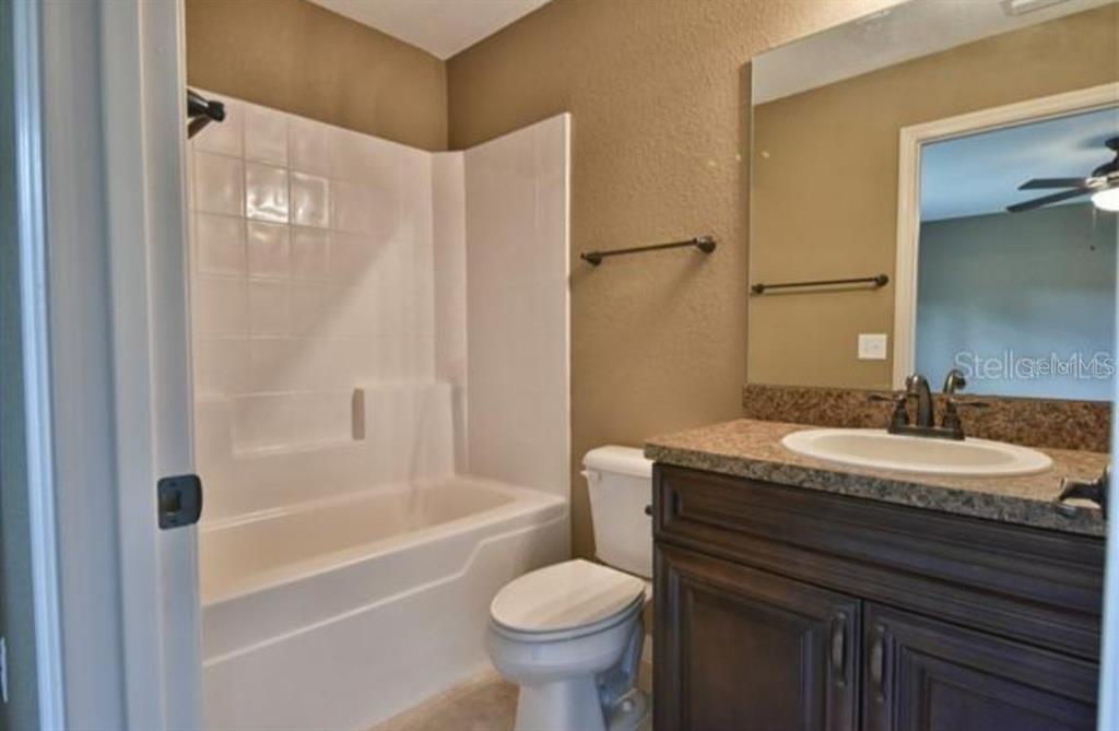 A bathroom features a white tub-shower combo, a toilet, and a dark wood vanity — 14196 SE 34TH TERRACE, SUMMERFIELD, FL