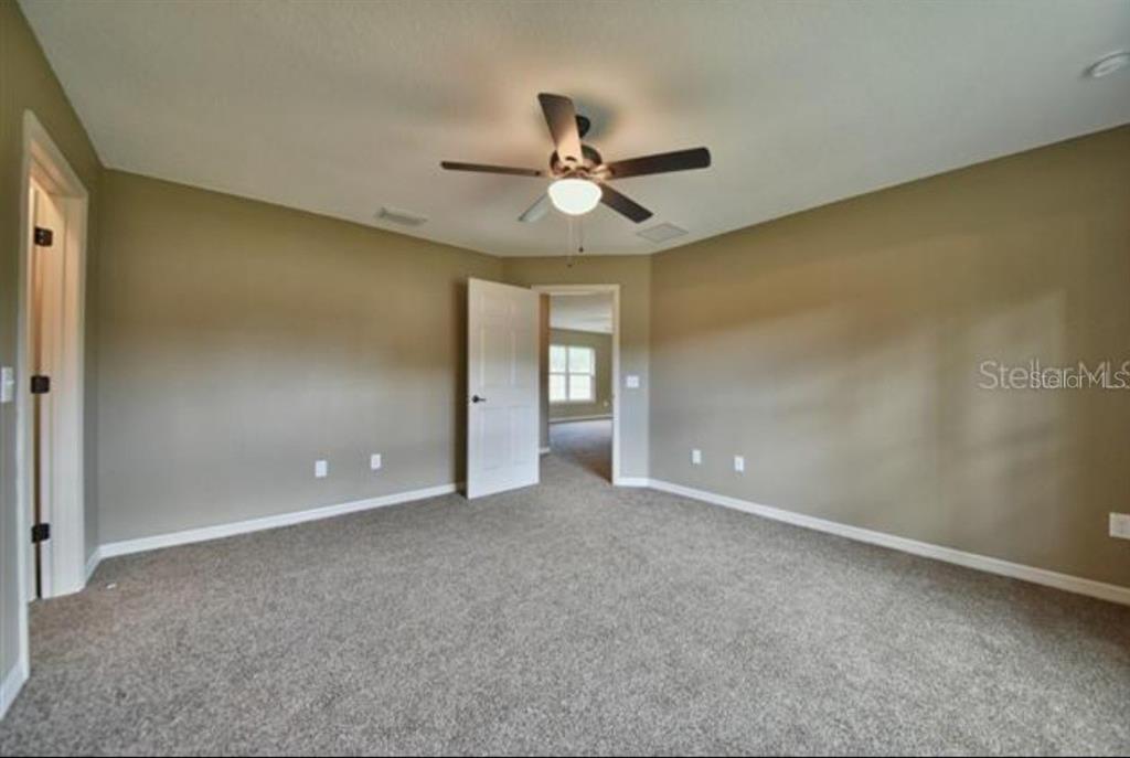 An empty bedroom features beige walls, gray carpeting, a ceiling fan, and two doorways — 14196 SE 34TH TERRACE, SUMMERFIELD, FL