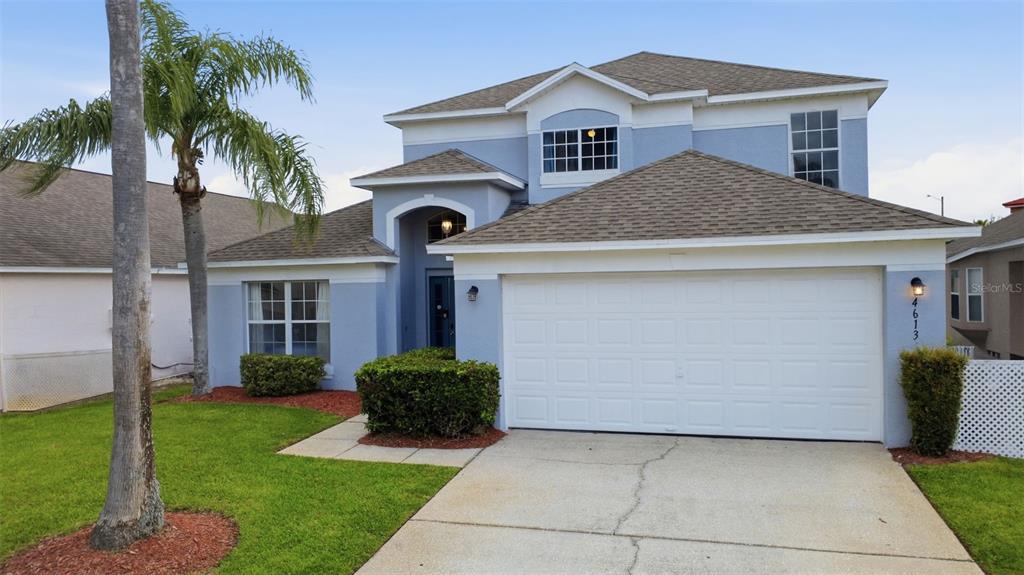 A two-story blue house with a white garage door, a palm tree, and landscaping — 4613 FORMBY COURT, KISSIMMEE, FL