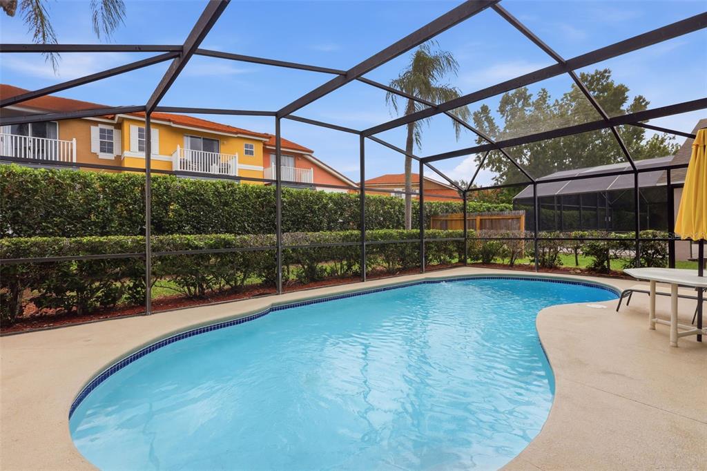 A swimming pool with a screened enclosure sits in a backyard next to apartment buildings — 4613 FORMBY COURT, KISSIMMEE, FL